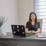 A woman sits at a desk with a laptop