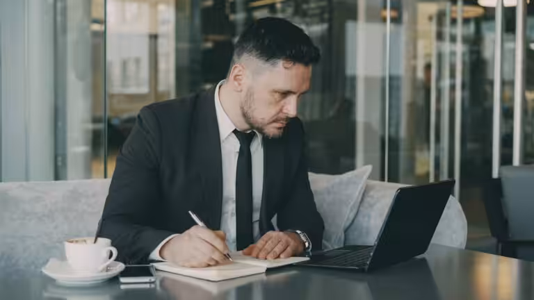 Man in suit writing in notebook at cafe table