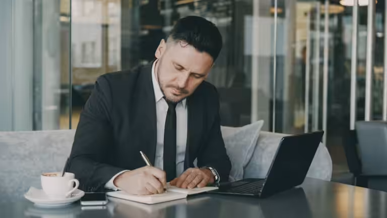 Man in suit writing in notebook at table